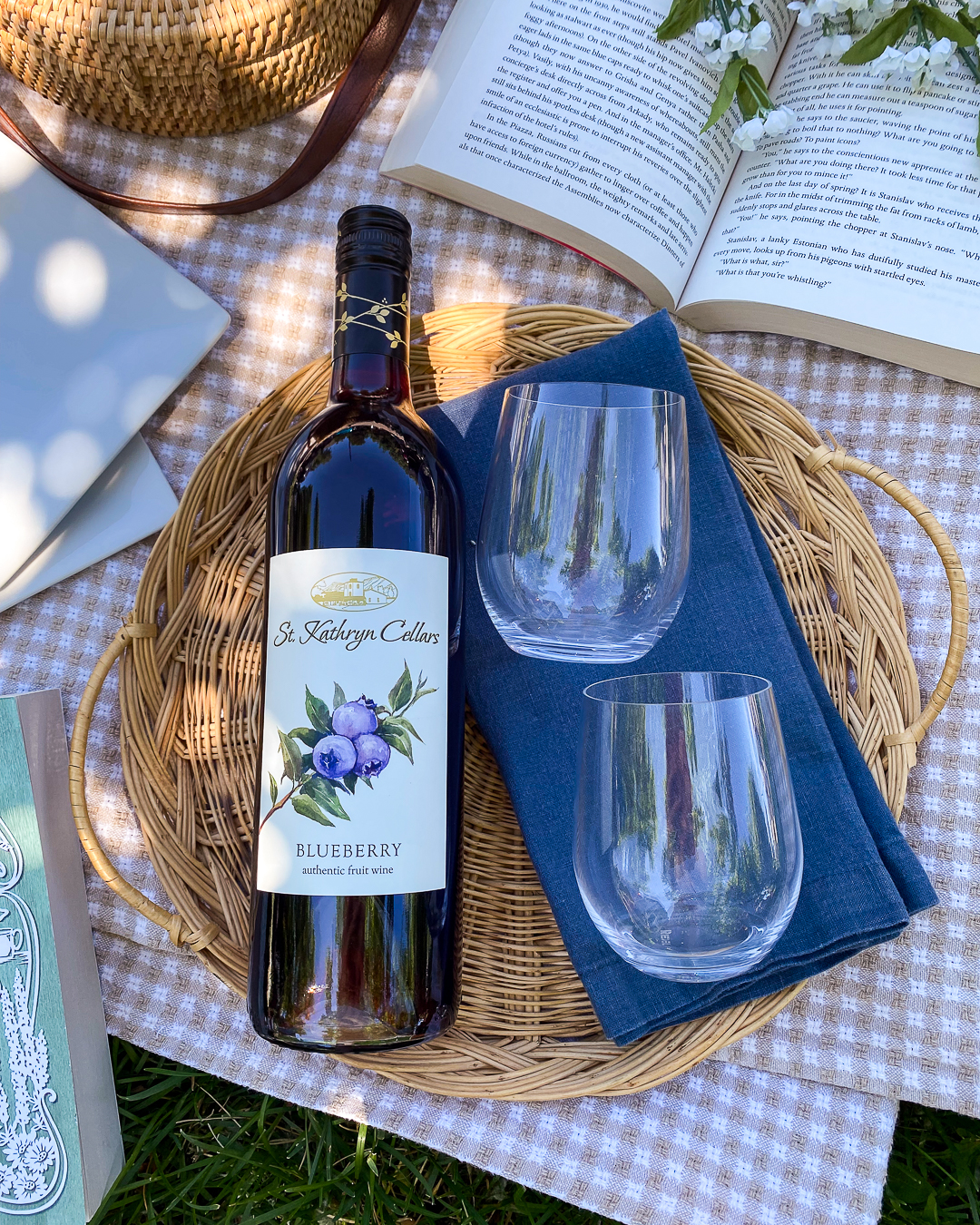 A bottle of blueberry wine with 2 empty wine glasses at a picnic scene